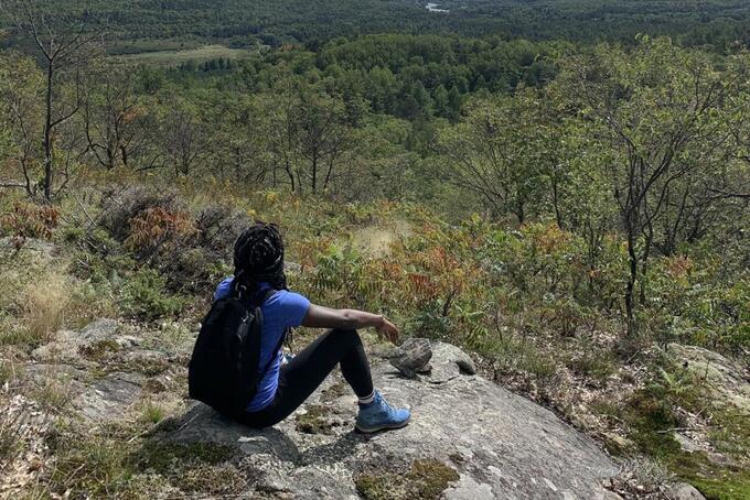 person sitting on rocky hillside looking down over forest view