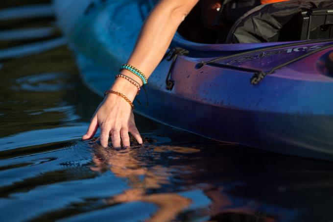 A woman dips her hand in the water while kayaking.