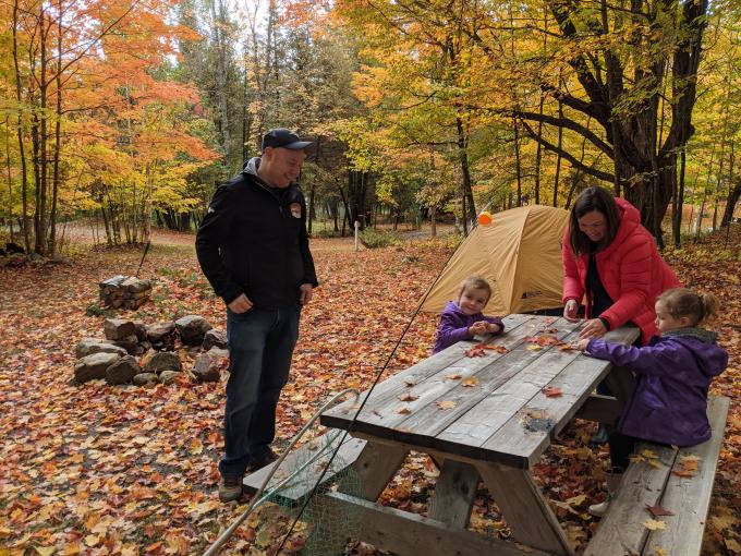 A man, woman, and two children are shown at a campsite in fall.
