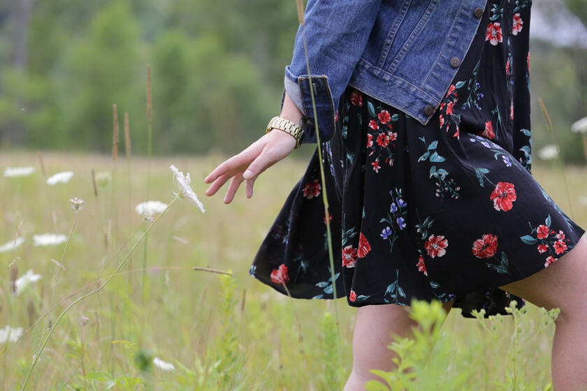 Girl in a dress and jacket walking through a field of flowers