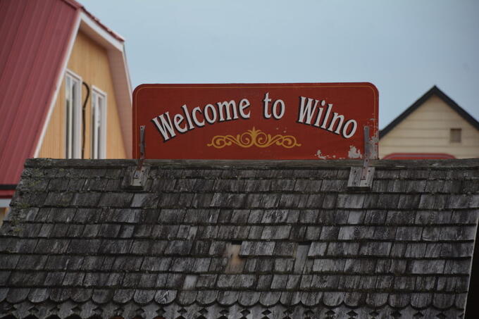 red sign over aged shake roof that reads "Welcome to Wilno"