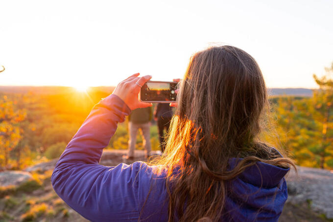 person in purple jacket holding up camera toward orange and gold sunrise