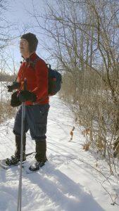 man in snowshoes standing on snowy forest trail