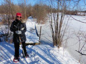 smiling woman wearing snowshoes on snowy forest trail