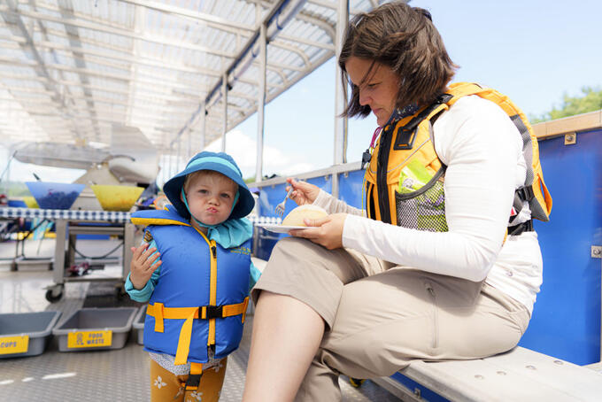 toddler in lifejacket being fed by parent