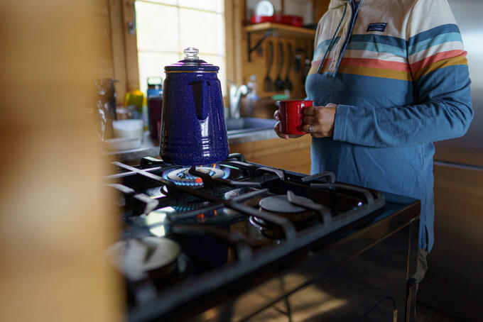 person in cabin making coffee on gas stove