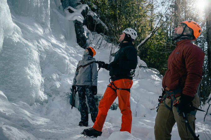 Lorne Foisy and two other people with sun and trees behind them, looking up at ice wall
