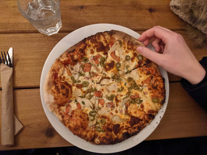 image of hand taking a slice of pizza off a white plate on a wooden table