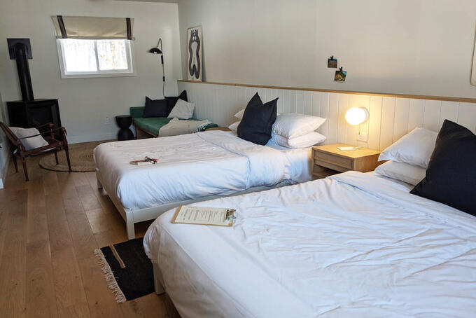 cozy inn room featuring wood stove and two large beds with white bedspreads and dark green pillows