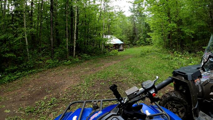 An ATV is parked in front of a small cabin in the woods.