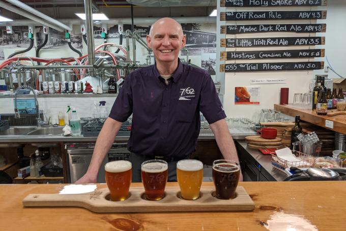 A man stands in front of a flight of 7/62 Craft Brewery beer.