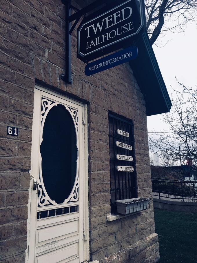 an old brick building with antique white wooden screen door, with a sign overhead that reads "Tweed Jailhouse Visitor Information"