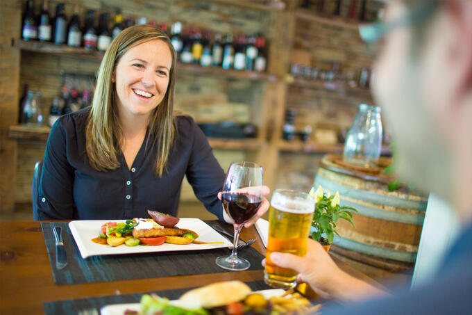 two people talking and smiling at a restaurant table, each with drinks in their hand and a plate of food in front of them