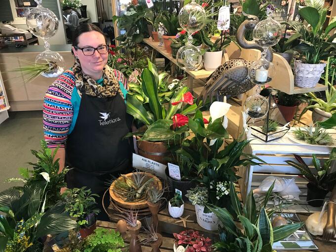 The owner of Gemmell's Flowers stands among plants in the store.