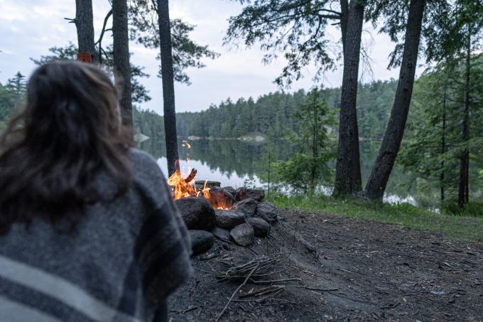 A woman sits in front of a campfire.