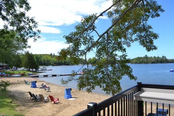 a sandy beach dotted with beach chairs and surrounded by green forest, blue lake water and blue sky