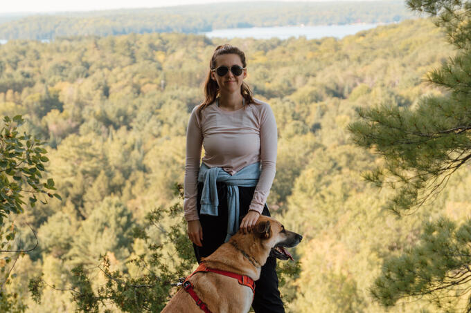 A woman and dog stand in front of a lookout over a forest.