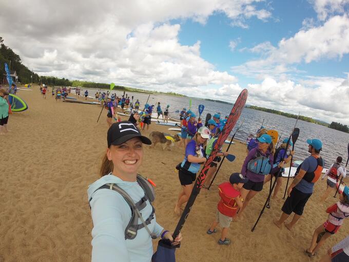 A woman stands on a beach holding a paddle.