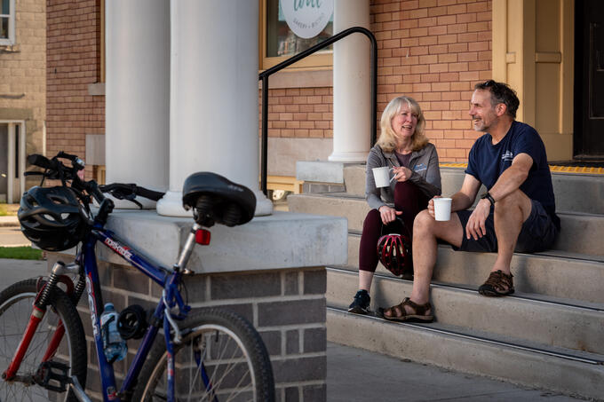 Two cyclists sit on steps with a cup of coffee