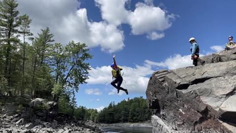 person in lifejacket jumping from rocky outcropping into water 