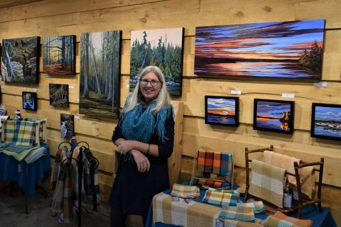 artist Wendy Wood smiling next to studio wall displaying rows of her paintings