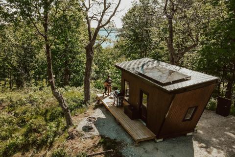 couple hugging on porch of tiny wooden cabin surrounded by forest