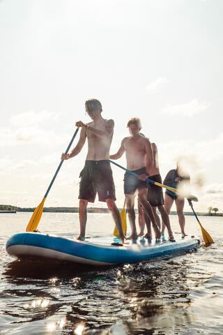Four young people stand on a sup paddle board on the water
