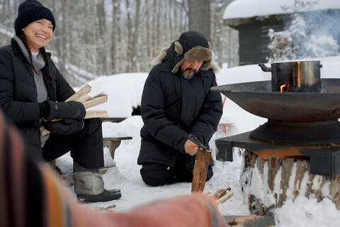 A man and woman build a fire outdoors in winter.