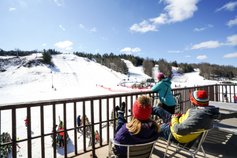 A group sits on a balcony overlooking a downhill skiing hill.