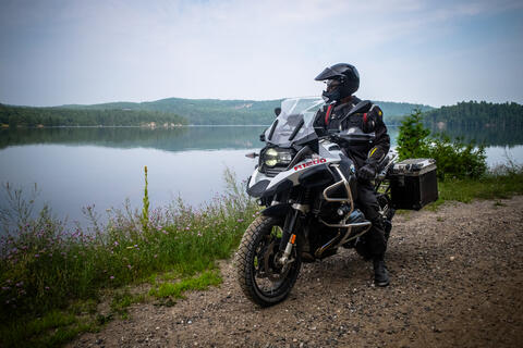 A man sits on a motorcycle beside a lake.