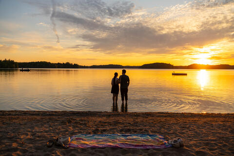 A couple stand on a beach at sunset