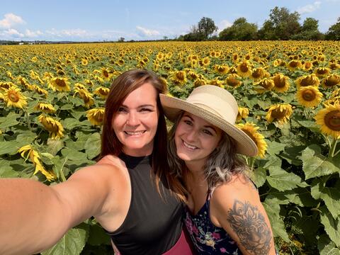 Two women standing in a field of sunflowers.